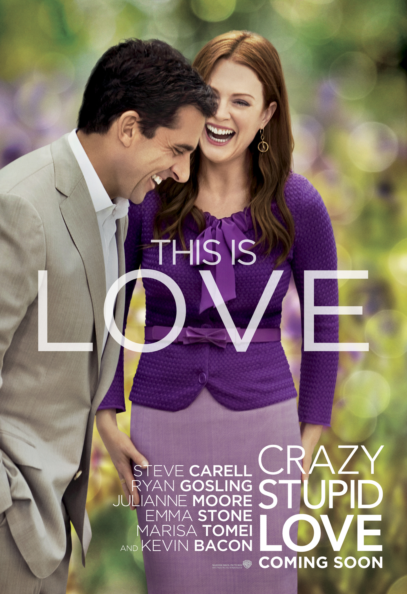Movie poster for Crazy, Stupid, Love. A man in a tan suit leans in laughing against a woman in a purple cardigan, who laughs toward the camera, both outdoors against blurred green and purple foliage. "This is love" appears in large white type across the center. The title runs down the lower right in white capitals.