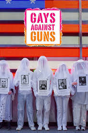 Movie poster for Gays Against Guns. A row of figures stands fully draped in white veils that hide their faces, each holding a portrait photograph against their chest. Behind them glows a large illuminated American flag. The title appears in bold multicolored letters inside a pink-bordered box.