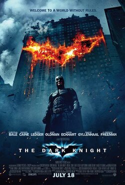 Movie poster for The Dark Knight. A masked figure in a dark armored suit and cape stands in the street at night, looking down. Behind him a skyscraper burns, the flames forming a bat shape across its face. The tagline "Welcome to a world without rules" runs along the top. The title appears near the bottom in white capitals. July 18.