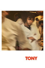 Movie poster for Tony. A young man portraying Anthony Bourdain stands with his arms crossed in a busy restaurant kitchen, wearing a white chef's jacket and looking directly at the camera while blurred figures rush past him. The tagline is a quote from him describing himself as "a spoiled, miserable, narcissistic, self-destructive and thoughtless young lout." The title appears in orange capitals at the bottom.